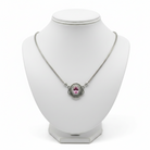 A silver-toned chain necklace with an oval pendant featuring a pink gemstone, displayed on a white jewelry bust against a white background.