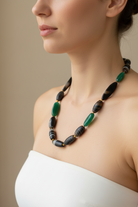 Necklace with green and black beads on a mannequin bust in a store window.